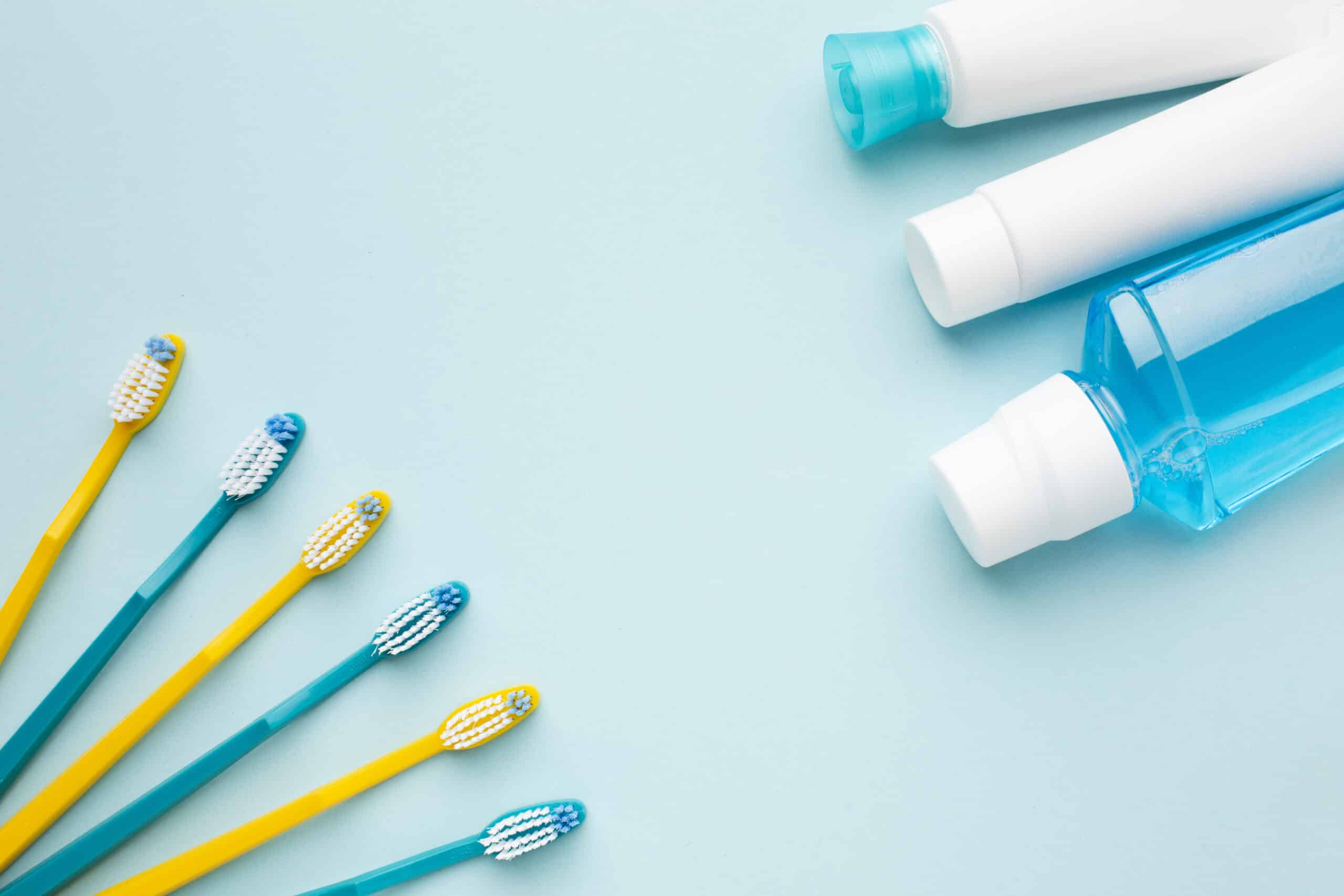 fotografia de producto con un fondo azul tenue. de lado izquierdo una fila de lentes y de lado derecho clorhexidina dental en frasco y en medio una plasta de dientes